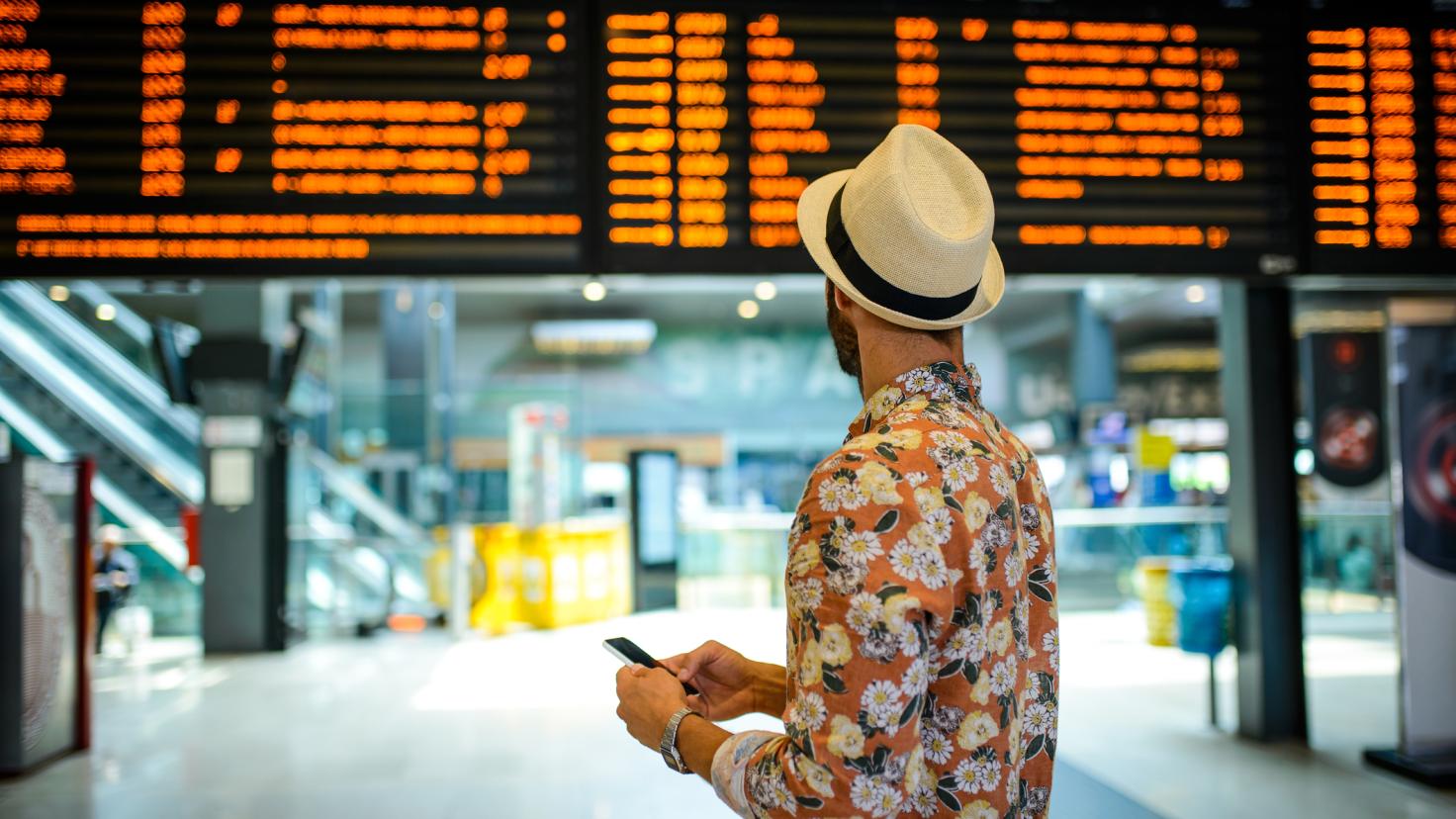 A man in a hat looks at a departures board in a station